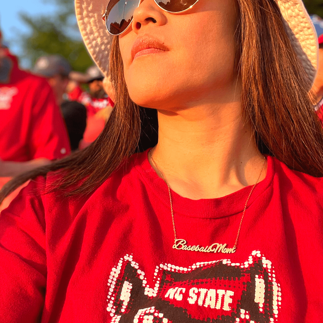 A life style product picture of Baseball Mom necklace. A model is wearing a Baseball Mom necklace at a baseball game. Side View