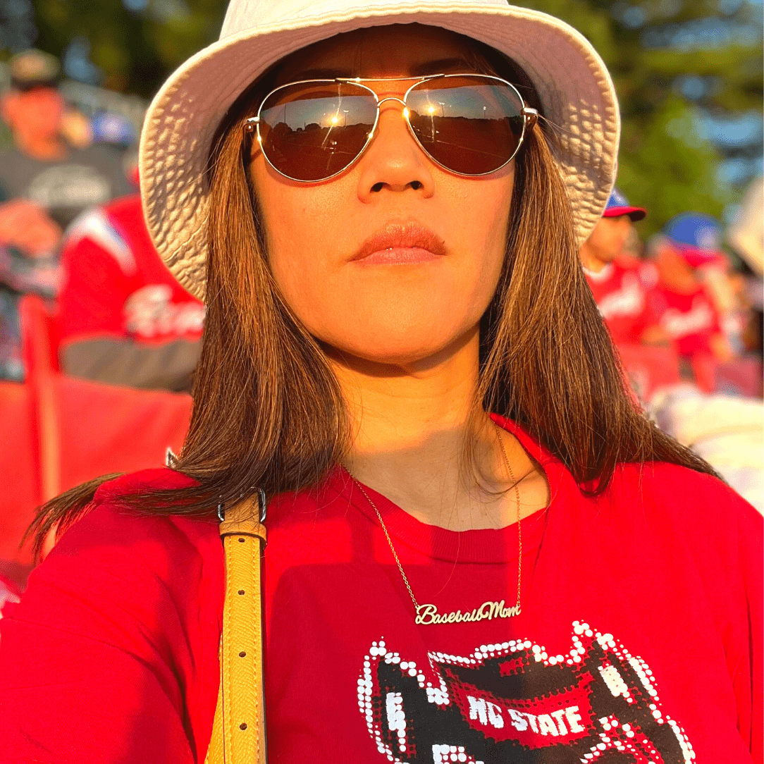 A life style product picture of Baseball Mom necklace. A model is wearing a Baseball Mom necklace at a baseball game
